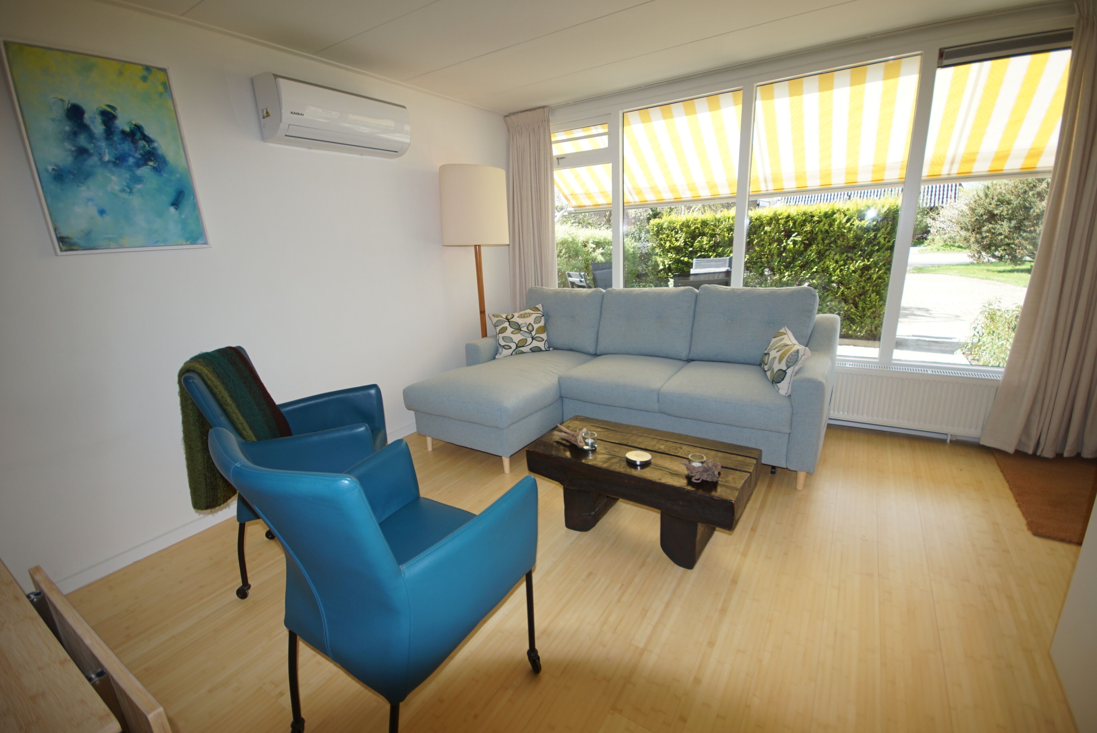 Een woonkamer met een blauwe bank, een blauwe fauteuil, een houten salontafel en een lamp.