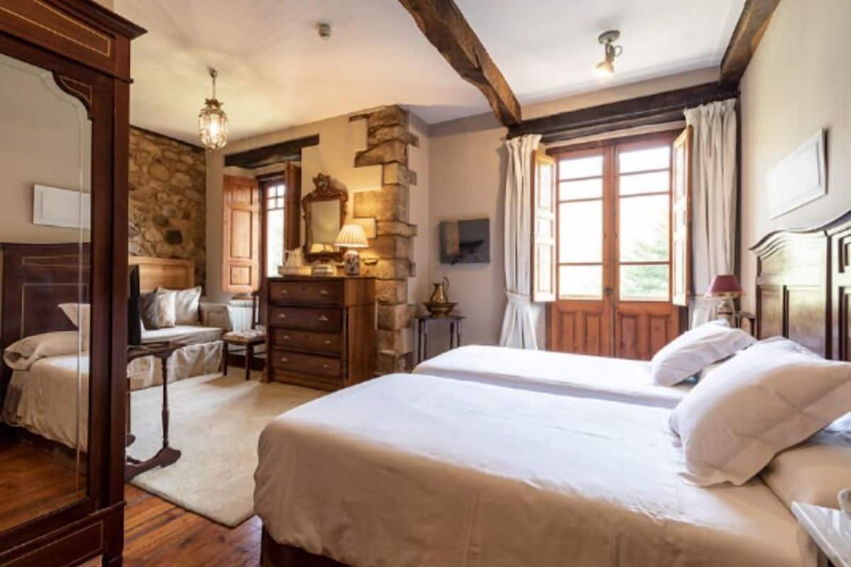 A bedroom with a stone wall, wooden furniture, a large bed, a dresser, and a mirror.
