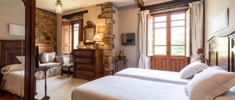 Une chambre avec un mur en pierre, des meubles en bois, un grand lit, une commode et un miroir.