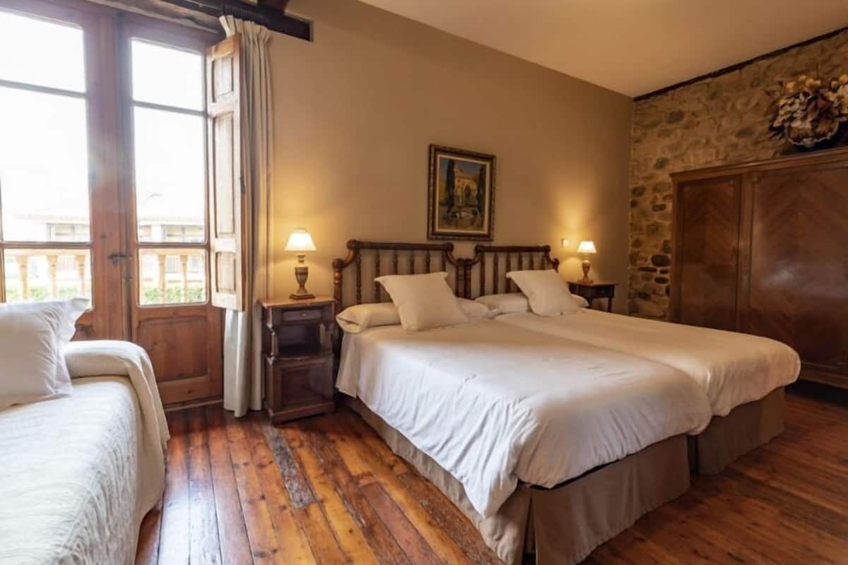 A hotel room with a large bed, a smaller bed, a wooden wardrobe, and a painting on the wall.