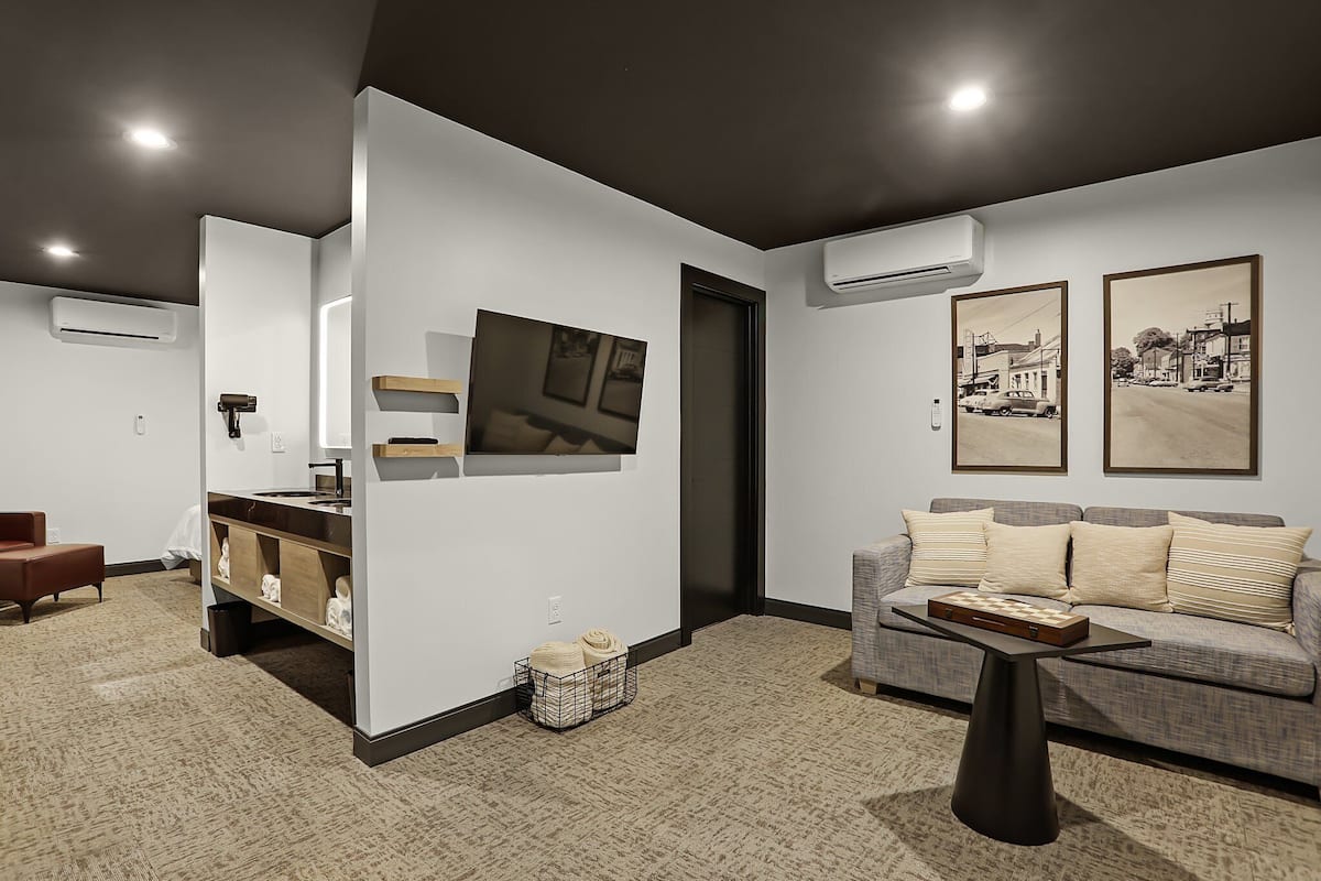 Un salon moderne avec un canapé, une table basse et un buffet. Deux tableaux encadrés ornent le mur, et un appareil de climatisation est fixé au mur.