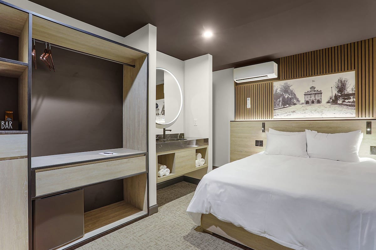 Une chambre d’hôtel comprenant un lit, une coiffeuse avec un miroir, un petit bureau et un climatiseur fixé au mur.
