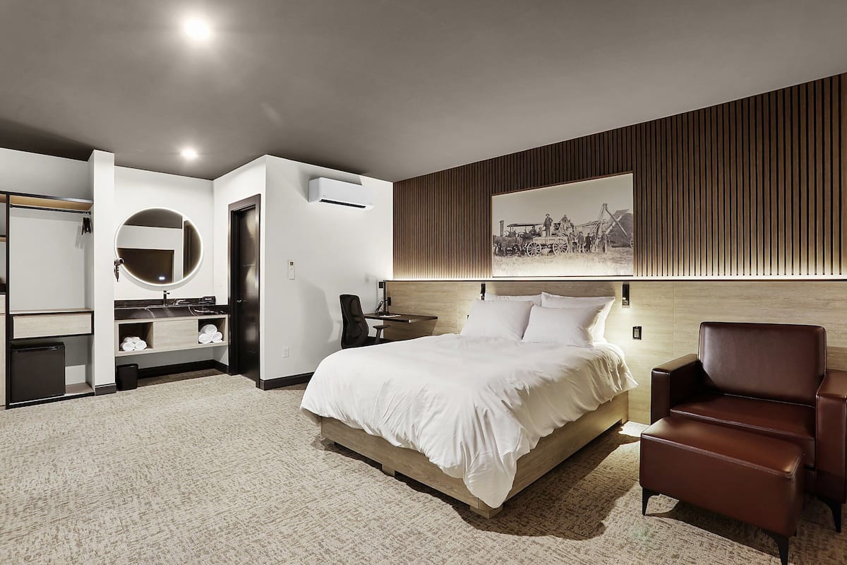 Une chambre d’hôtel moderne avec un grand lit, une tête de lit en bois, un miroir rond, un bureau et une chaise.