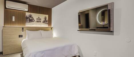 Ein Hotelzimmer mit einem Bett, einem Wandfernseher, einer Klimaanlage und einem gerahmten Bild an der Wand.
