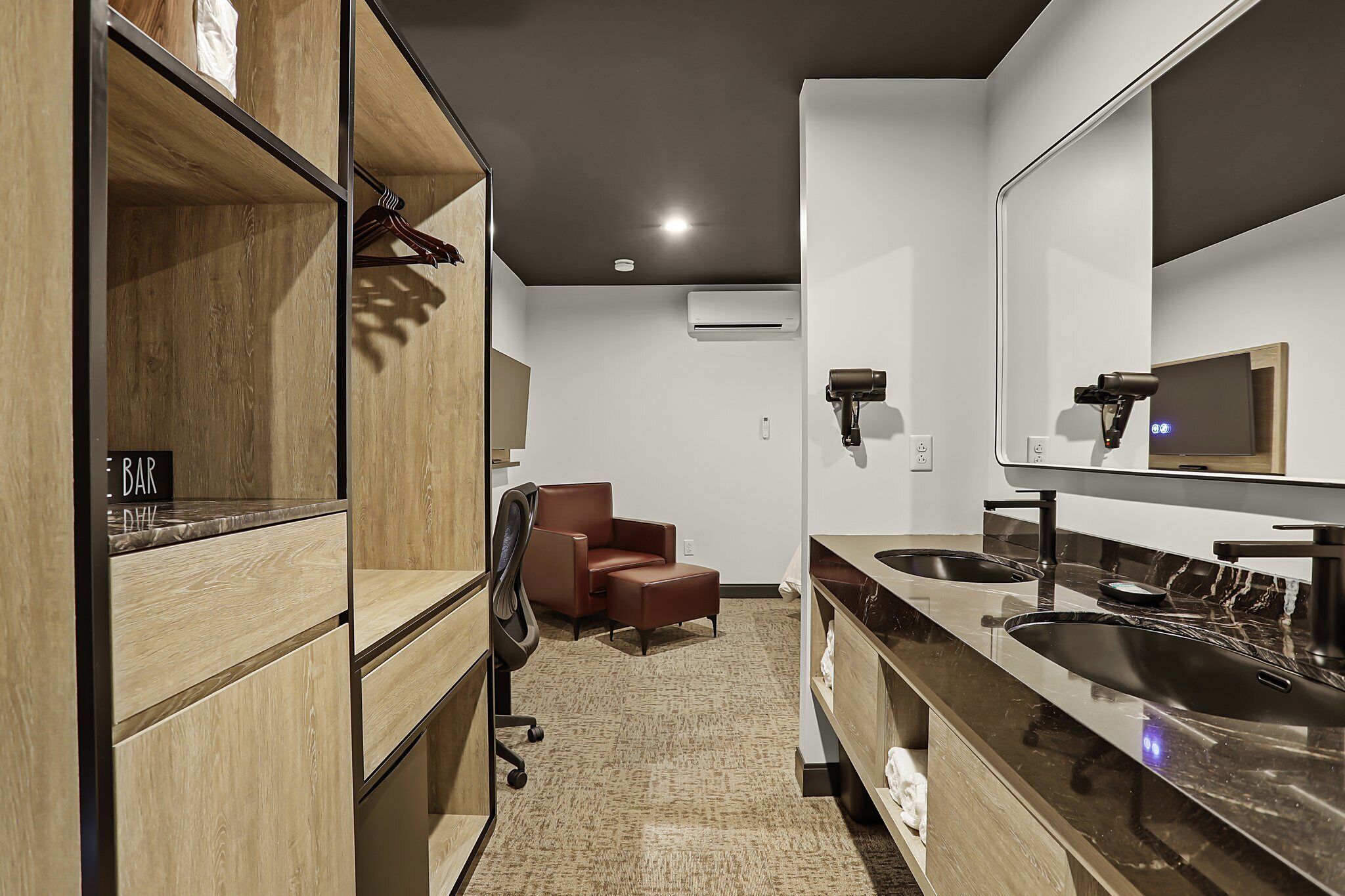 A modern bathroom with a large mirror, two sinks, and a chair.