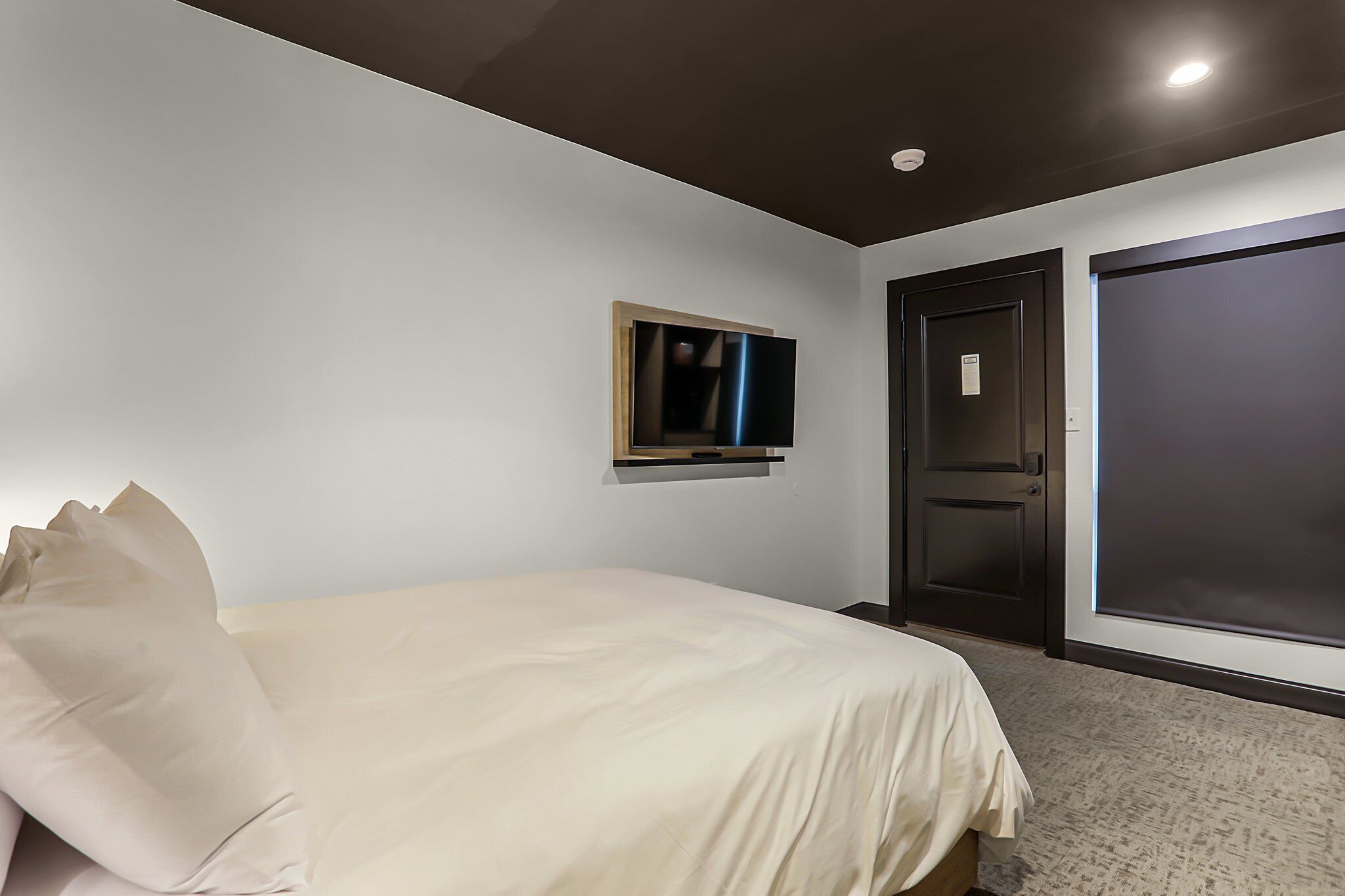 Una habitación de hotel con una cama, un televisor montado en la pared y una puerta.