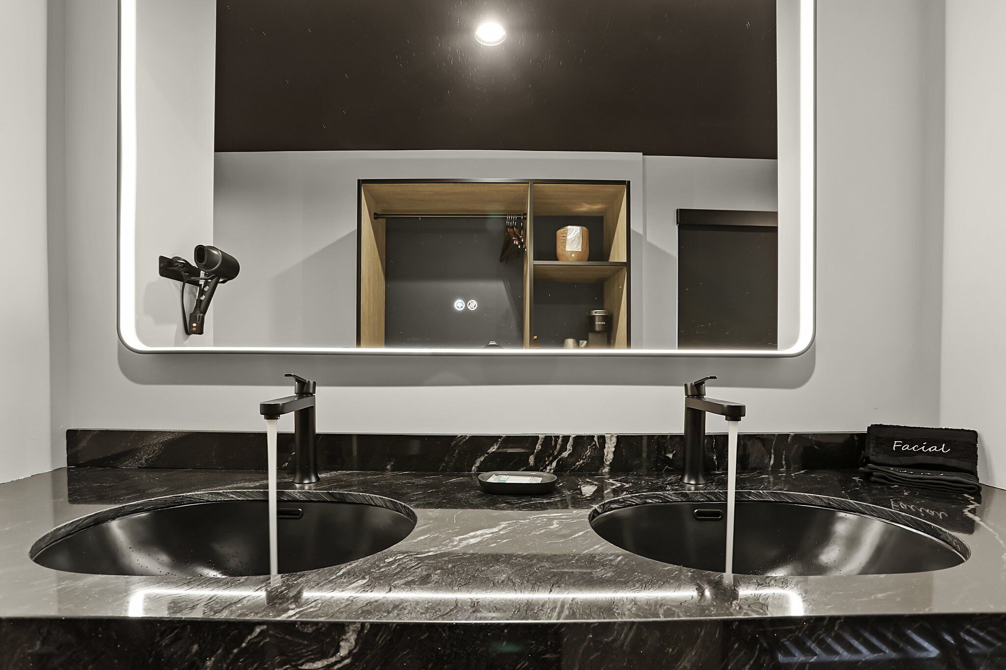 A bathroom with a double sink, a mirror, and a shelf with toiletries.