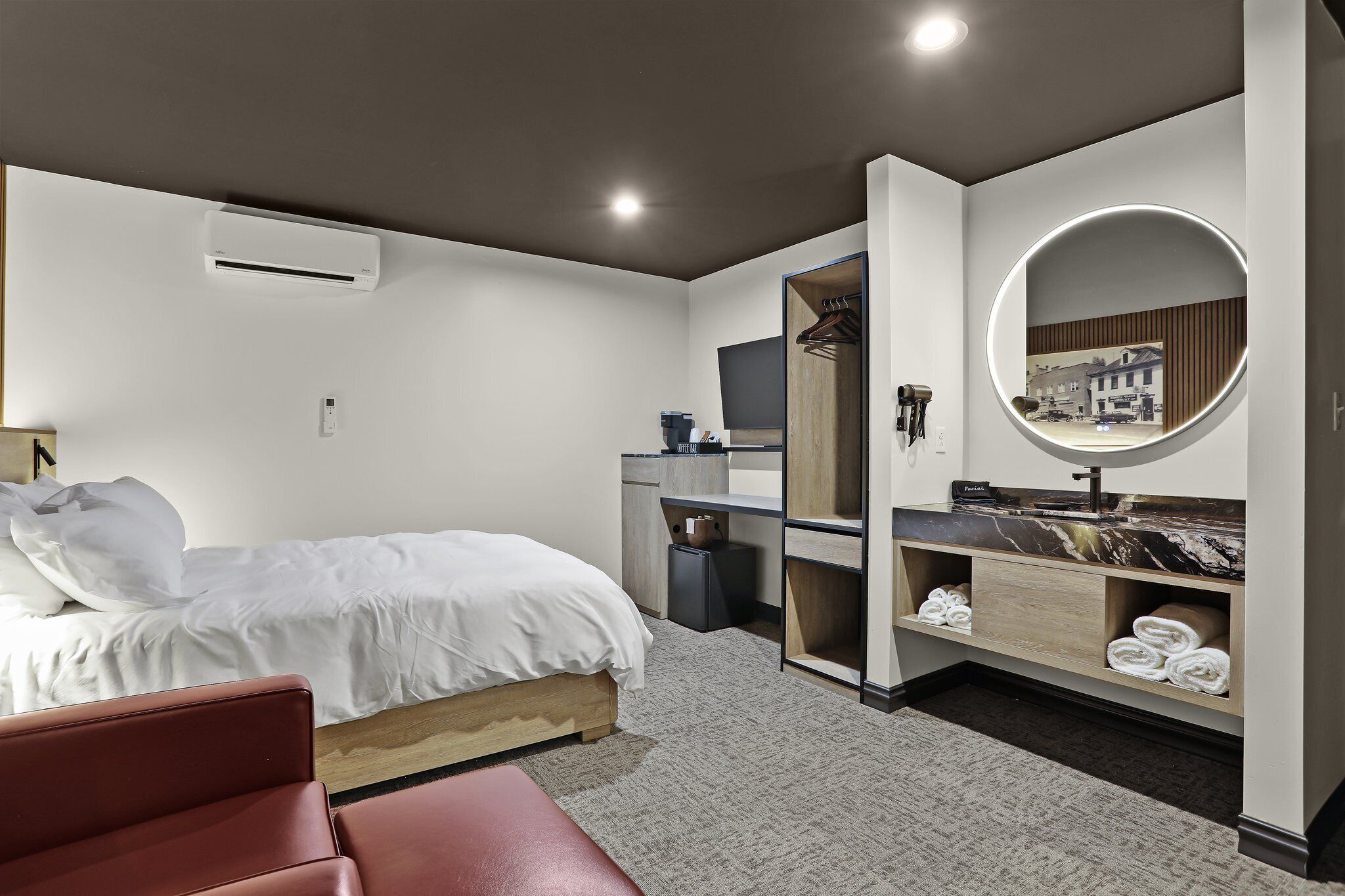 A modern hotel room with a bed, a vanity with a mirror, a small desk, and a red chair.