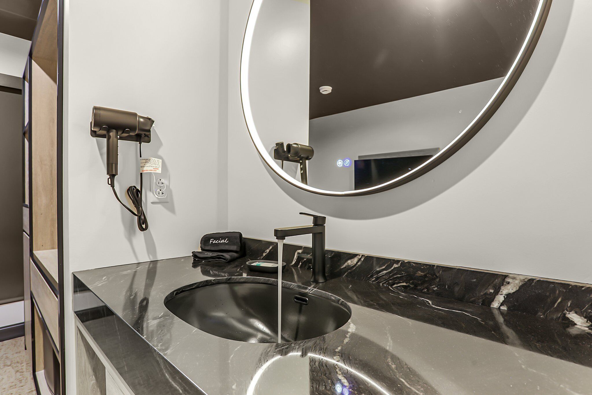 A modern bathroom with a black sink, a round mirror, and a hairdryer mounted on the wall.