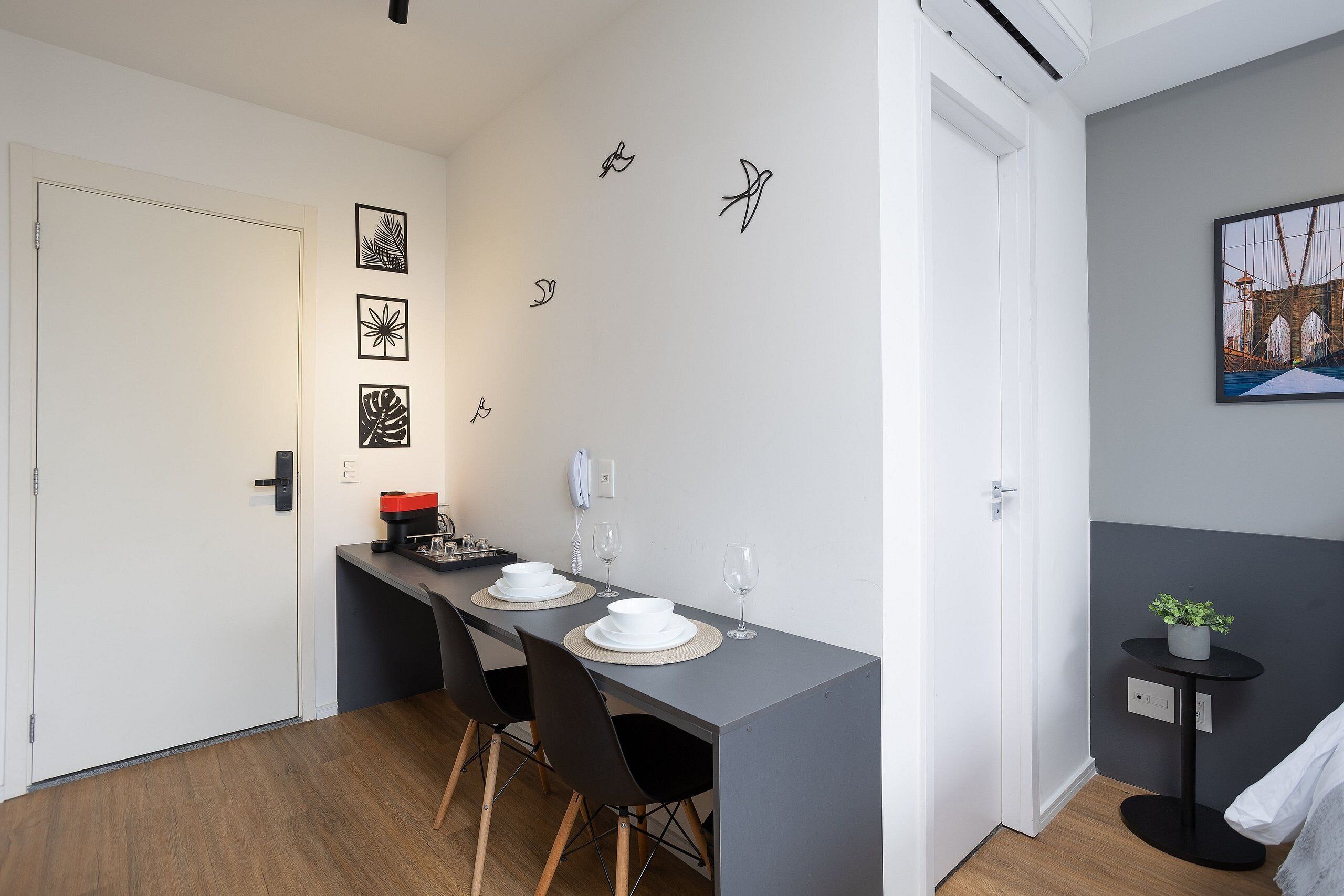 A modern dining area with a grey table, black chairs, and a small side table with a plant.