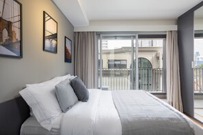 Une chambre d’hôtel avec un grand lit, un balcon donnant sur la ville et des œuvres d’art accrochées aux murs.