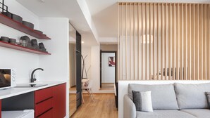 Eine moderne Küche mit roten Schränken, einer weißen Arbeitsplatte und einem eingebauten Ofen. Es gibt eine Holzwand mit vertikalen Lamellen und ein graues Sofa mit Kissen.