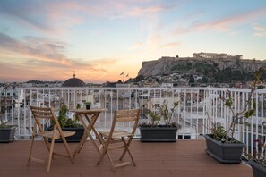 Une terrasse dotée de chaises et d’une table en bois, offrant une vue sur un paysage urbain historique, avec d’anciennes ruines.