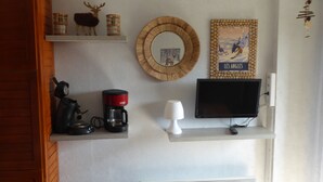 A living room with a coffee maker, a television, a decorative mirror, and a framed picture on the wall. - Studio apartment  Les Airelles residence  parking ski locker  balcony  lake view (Les Angles)