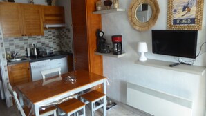 A compact kitchen with wooden cabinets, a coffee maker, and a TV on a shelf.