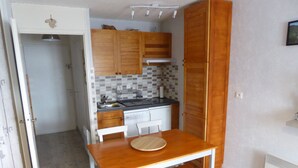 A compact kitchen with wooden cabinets, a white countertop, and a dining table with two chairs.