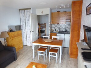 Un espacio habitable compacto con kitchenette, una zona de comedor con mesa y sillas, un sofá y un televisor.