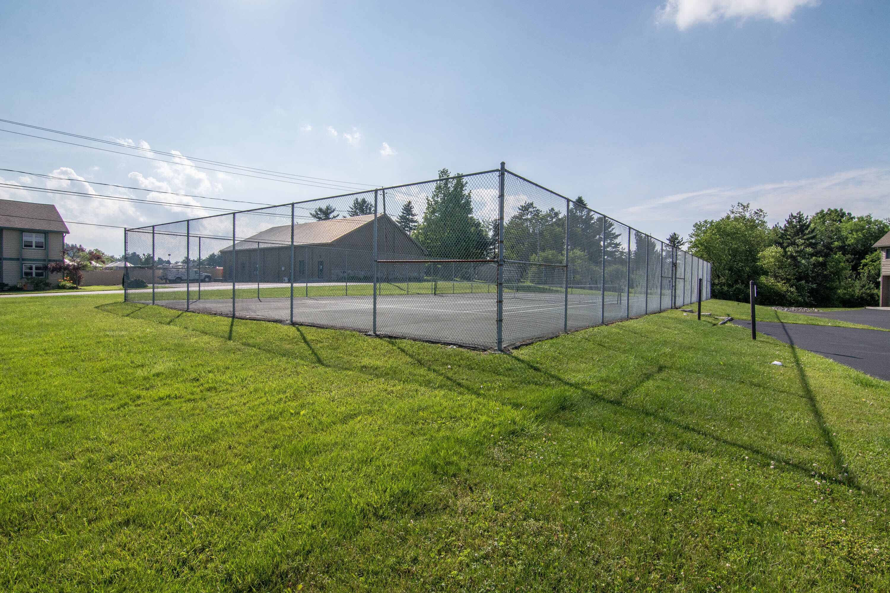 Una cancha deportiva cercada, con cielo despejado y casas al fondo.