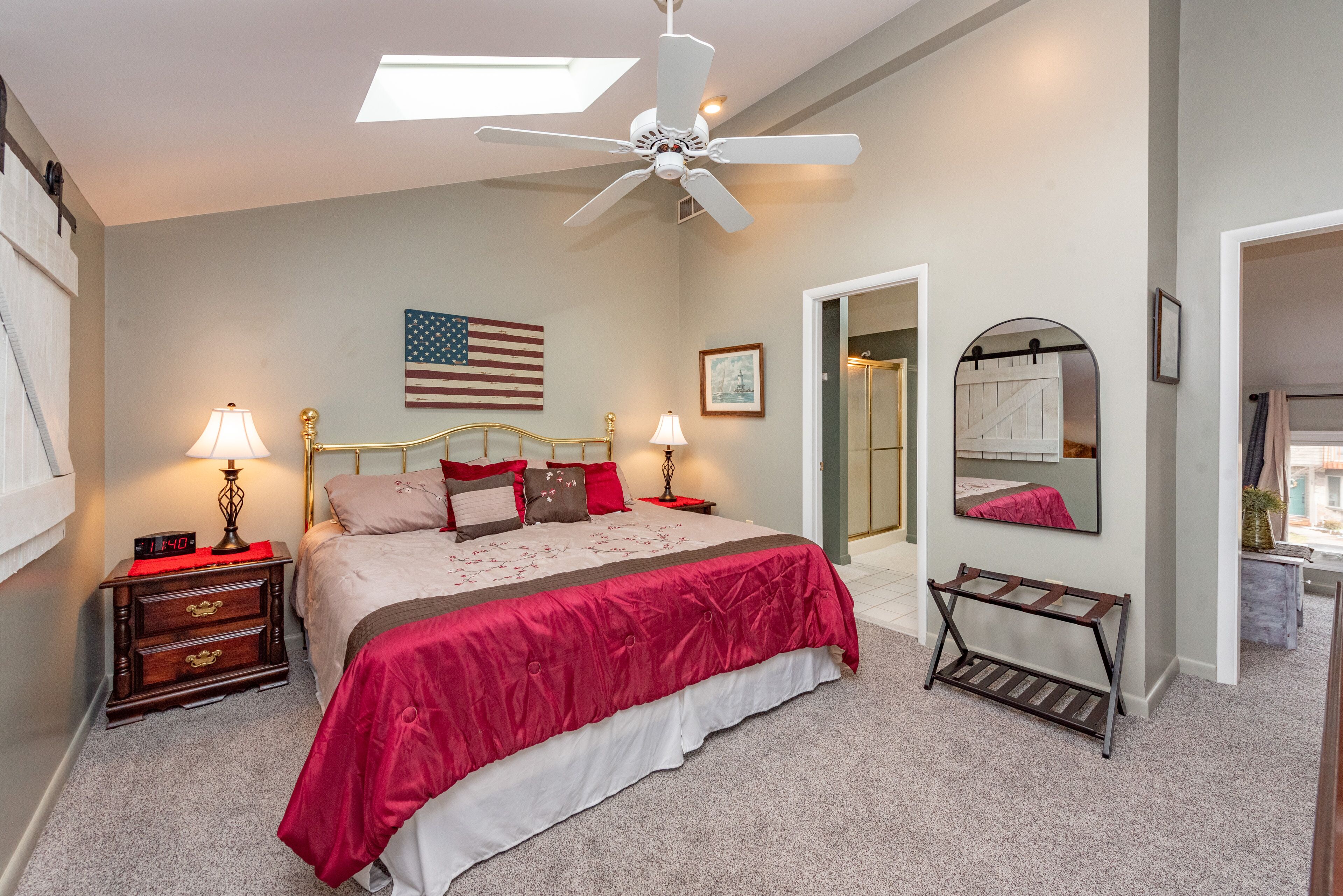 A bedroom with a bed, nightstands, a ceiling fan, an American flag, a mirror, and a door leading to another room.