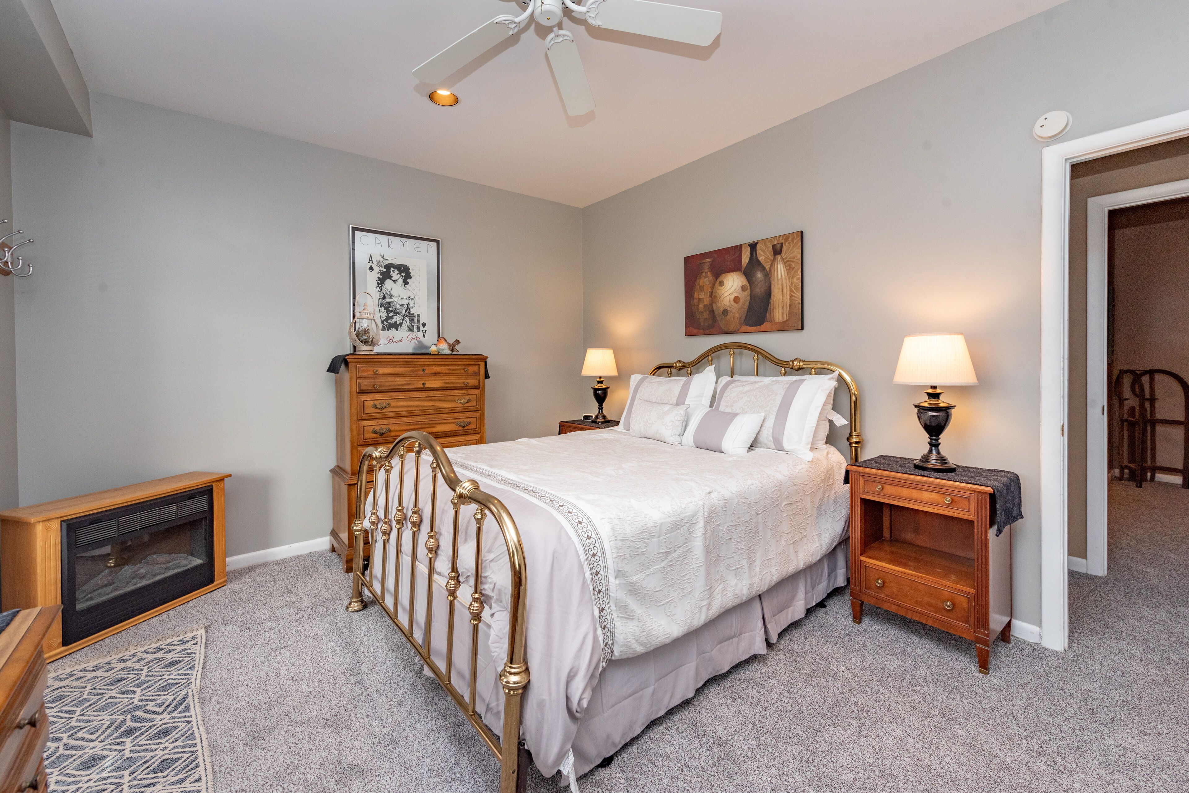 Une chambre à coucher comprenant un lit, des tables de chevet, une commode, un ventilateur de plafond et une cheminée.