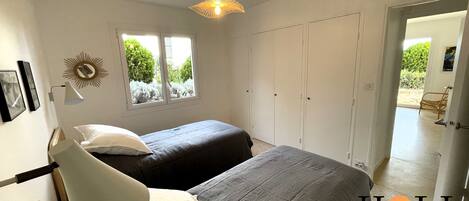 A bedroom with two beds, a window, a wardrobe, and a door leading to a balcony.