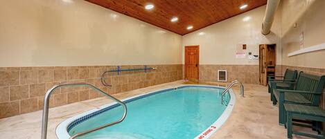 Ein Hallenbad mit Holzbalkendecke, gefliesten Wänden und einer Sitzgelegenheit am Beckenrand.