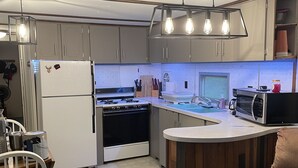 Eine moderne Küche mit Einbauofen, Kühlschrank, Mikrowelle und Spüle. Eine Holzinsel mit einem Stuhl, darüber eine Leuchte.
