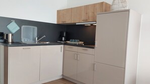 A modern kitchen with light wood cabinets, a stainless steel sink, and a white refrigerator. - 2-room vacation apartment directly on Lake Constance with bathing area (Überlingen)