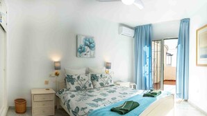 Ein Schlafzimmer mit Bett, Nachttischen, einer Wand-Klimaanlage und Blick ins Freie durch eine Tür.