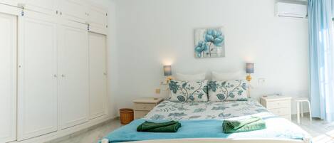 A bedroom with a bed, nightstands, a wall-mounted air conditioner, and a large wardrobe.