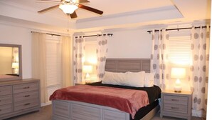 A bedroom with a bed, nightstands, a dresser, a ceiling fan, and curtains.