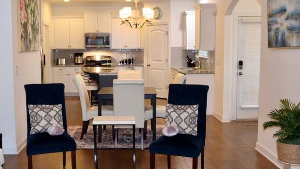 A modern kitchen with white cabinets, a central island, and a chandelier. There are two chairs with patterned cushions and a dining table.