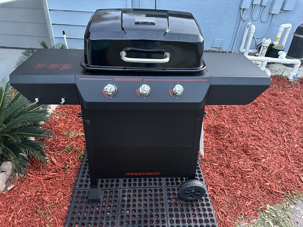 Un barbecue d’extérieur noir, portant la marque « megamaster », doté d’une poignée et de trois boutons de contrôle.