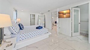 Ein modernes Schlafzimmer mit einem großen Bett, einer Nachttischlampe und Blick auf den Flur.