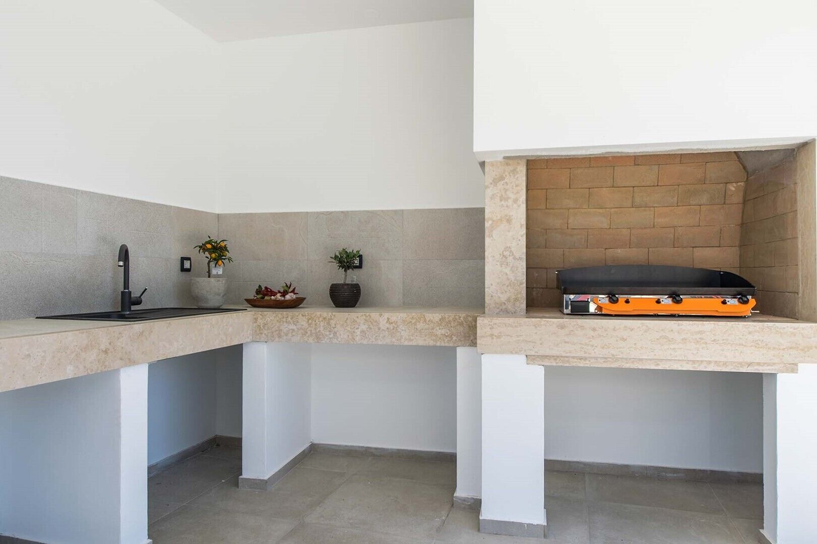 A compact kitchen with a built-in sink, two potted plants, and a small countertop with a grill.
