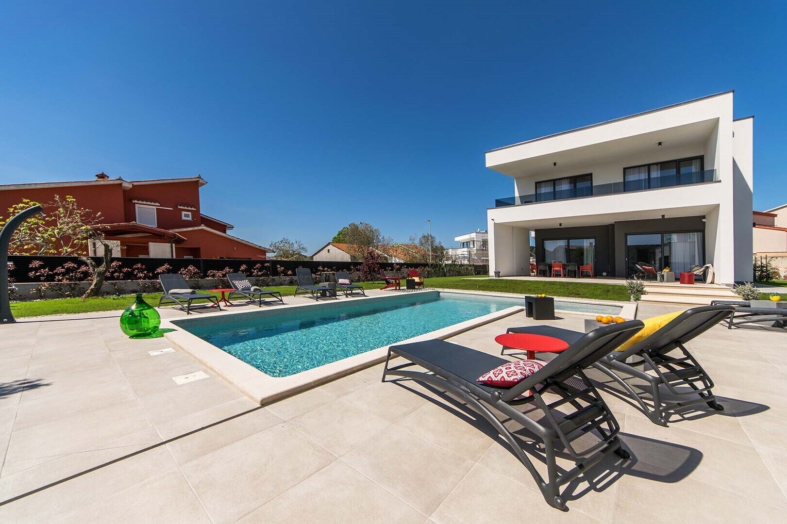 Uma área de piscina moderna ao ar livre, com espreguiçadeiras e um edifício contemporâneo ao fundo.
