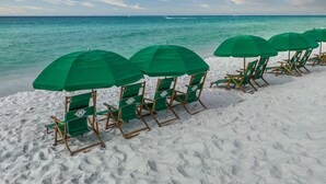 Een rij groene strandstoelen en parasols op een zandstrand, met uitzicht op de oceaan.
