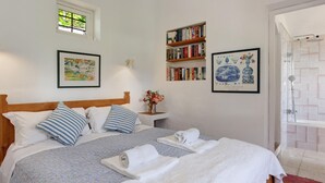 Un letto rifatto con cura, con una testiera in legno, un comodino con un vaso di fiori e una libreria piena di libri.