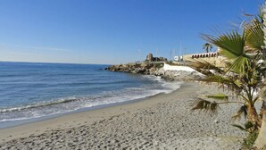 Una spiaggia con un litorale roccioso, palme e un edificio con archi.