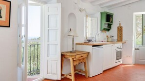 A kitchen with white cabinets, a wooden table, a green hanging shelf, and a view of the outdoors. - The Little Well: Private Pool, Sleeps2, Views (Frigiliana)