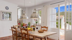 A dining area with a wooden table, chairs, and hanging pendant lights. There is a window with a view of the outdoors. - The Old Mill: Pool, Sleeps 8, WiFi, 4 bed, views (Frigiliana)