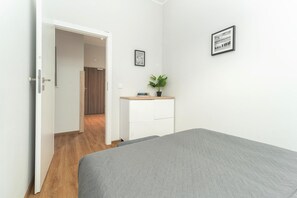 A bedroom with a bed, a dresser, a potted plant, and a door leading to another room. - Comfortable holiday apartment by the beach (Pobierowo)