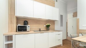 A modern kitchen with white cabinets, a microwave, a sink, and a vase with flowers. - Comfortable holiday apartment by the beach (Pobierowo)
