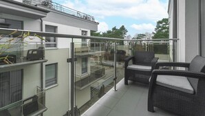 A balcony with wicker furniture and glass railings, overlooking a residential area. - Comfortable holiday apartment by the beach (Pobierowo)