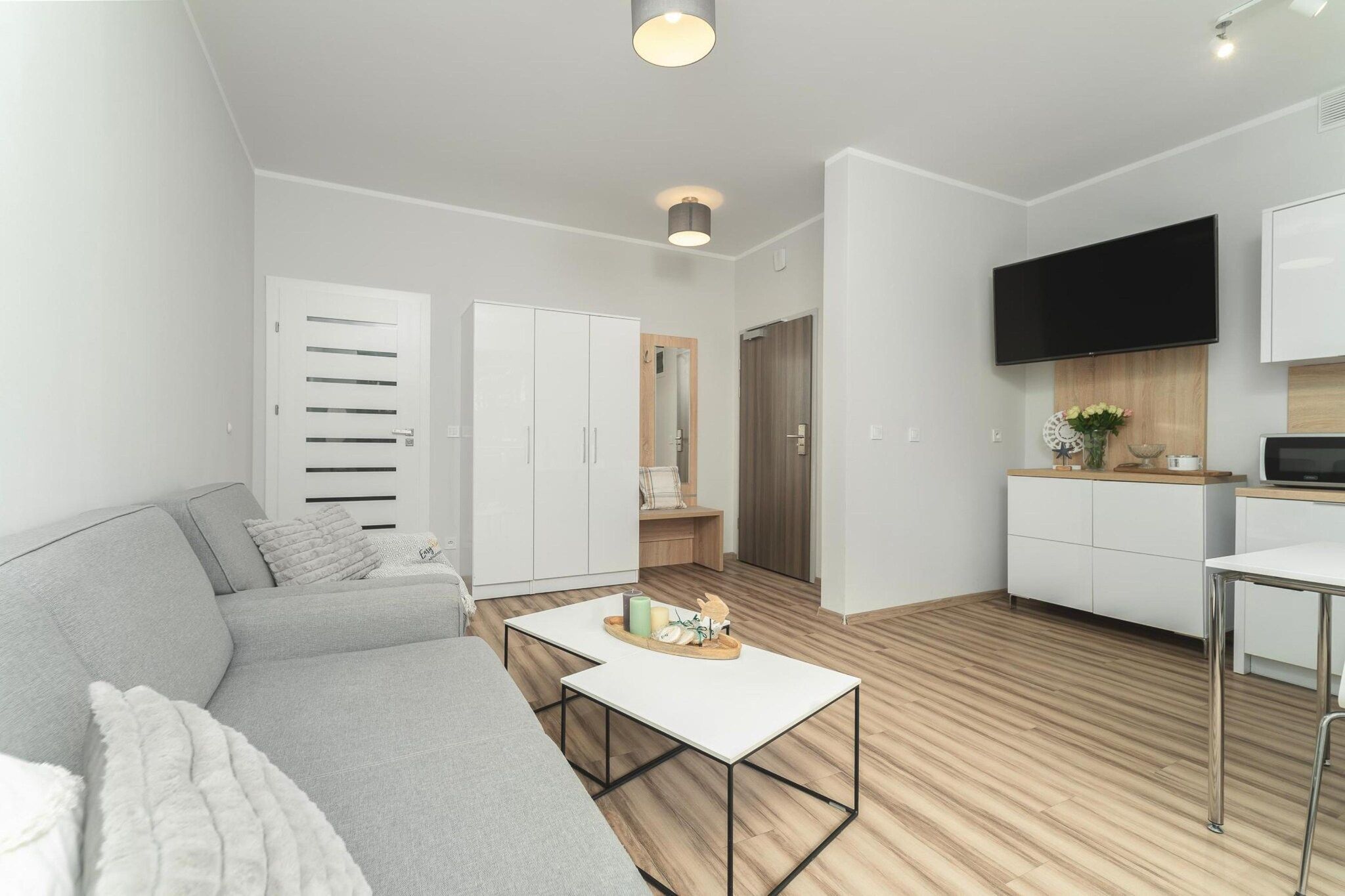 Ein modernes Wohnzimmer mit einem grauen Sofa, einem weißen Couchtisch und einer Küchenzeile inklusive Fernseher und Schränken.