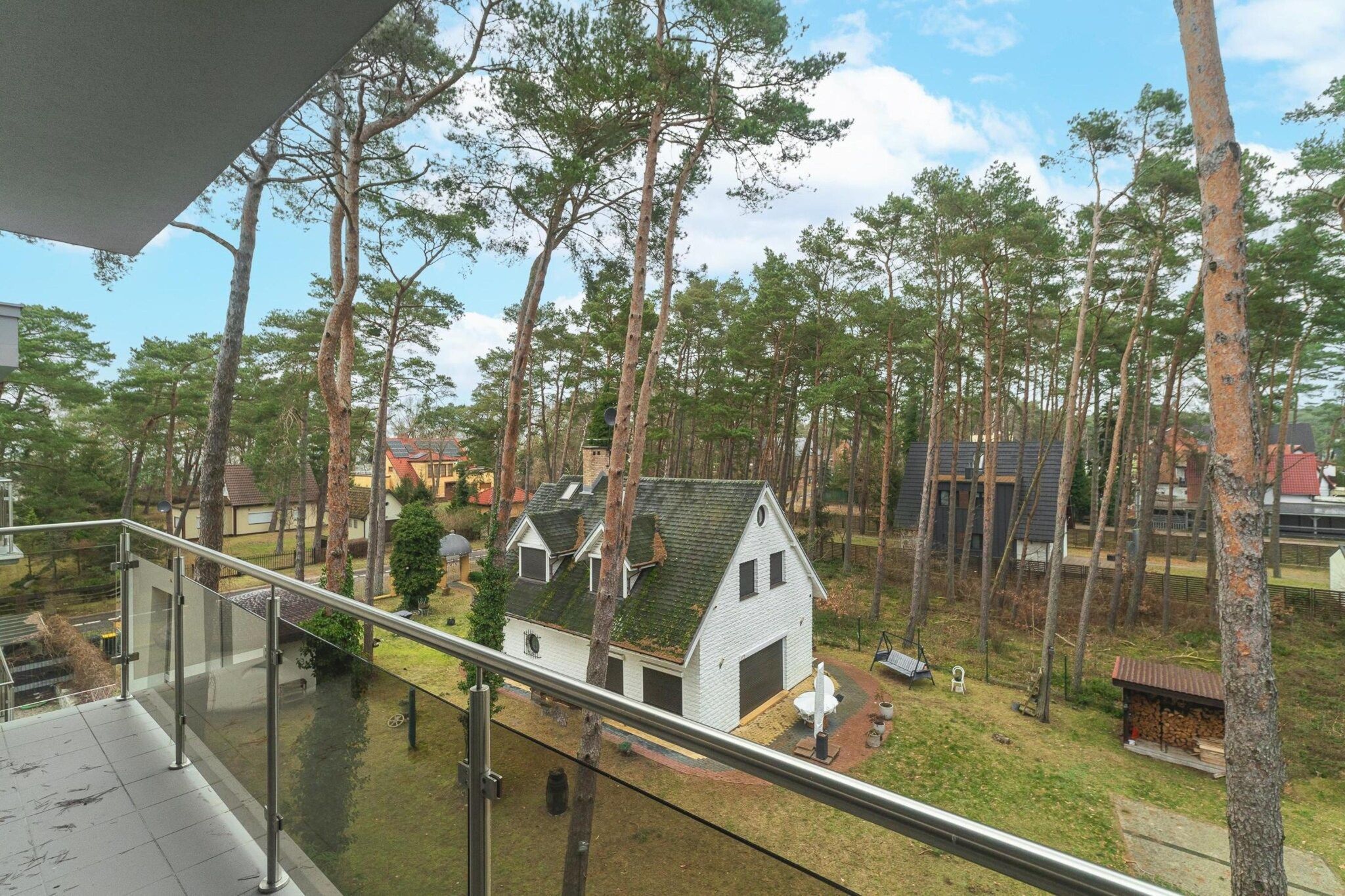 A residential area with a small white house surrounded by tall trees.