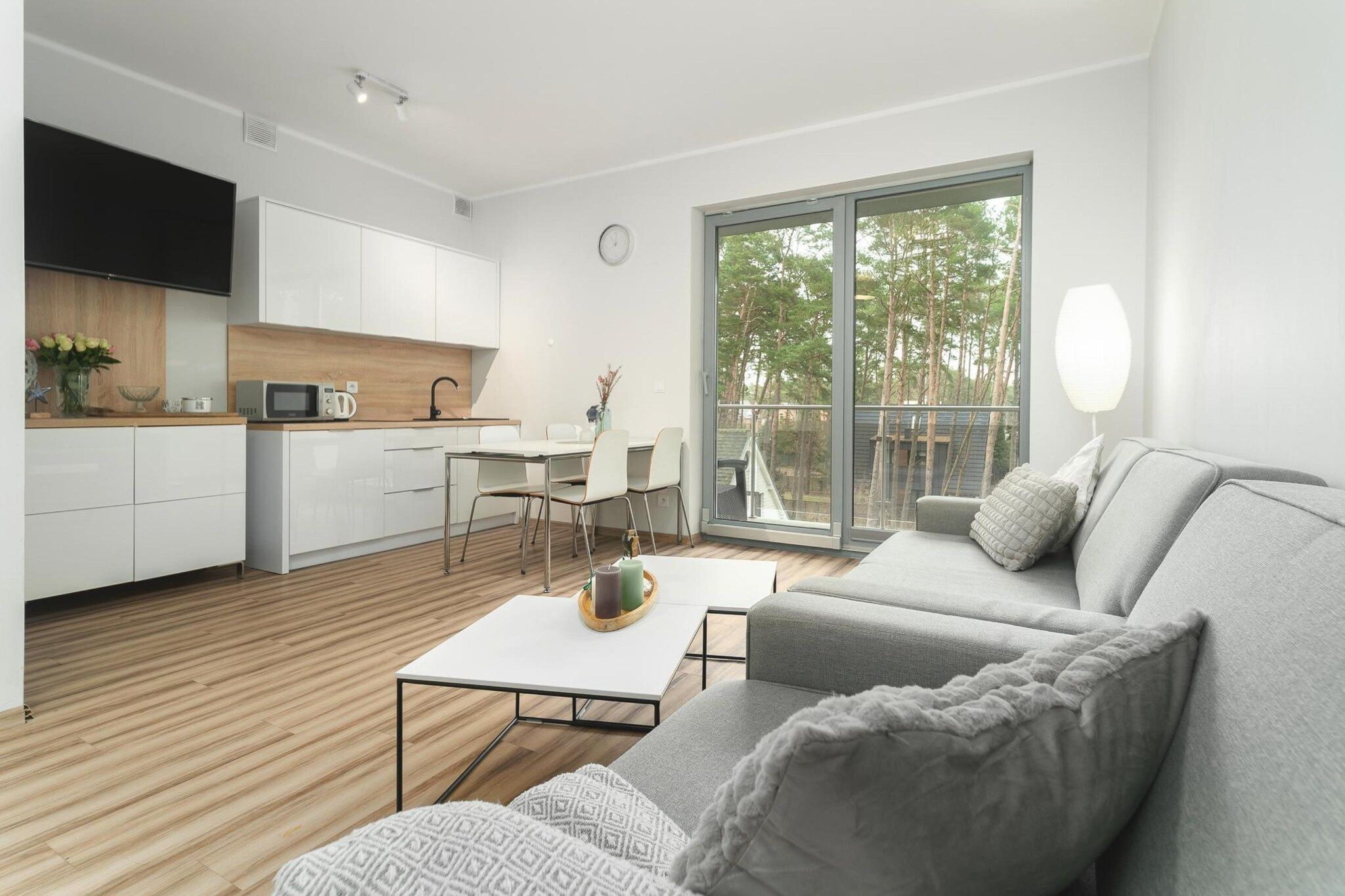 A modern living room with a grey sofa, a white coffee table, and a kitchen area with white cabinets and a microwave.