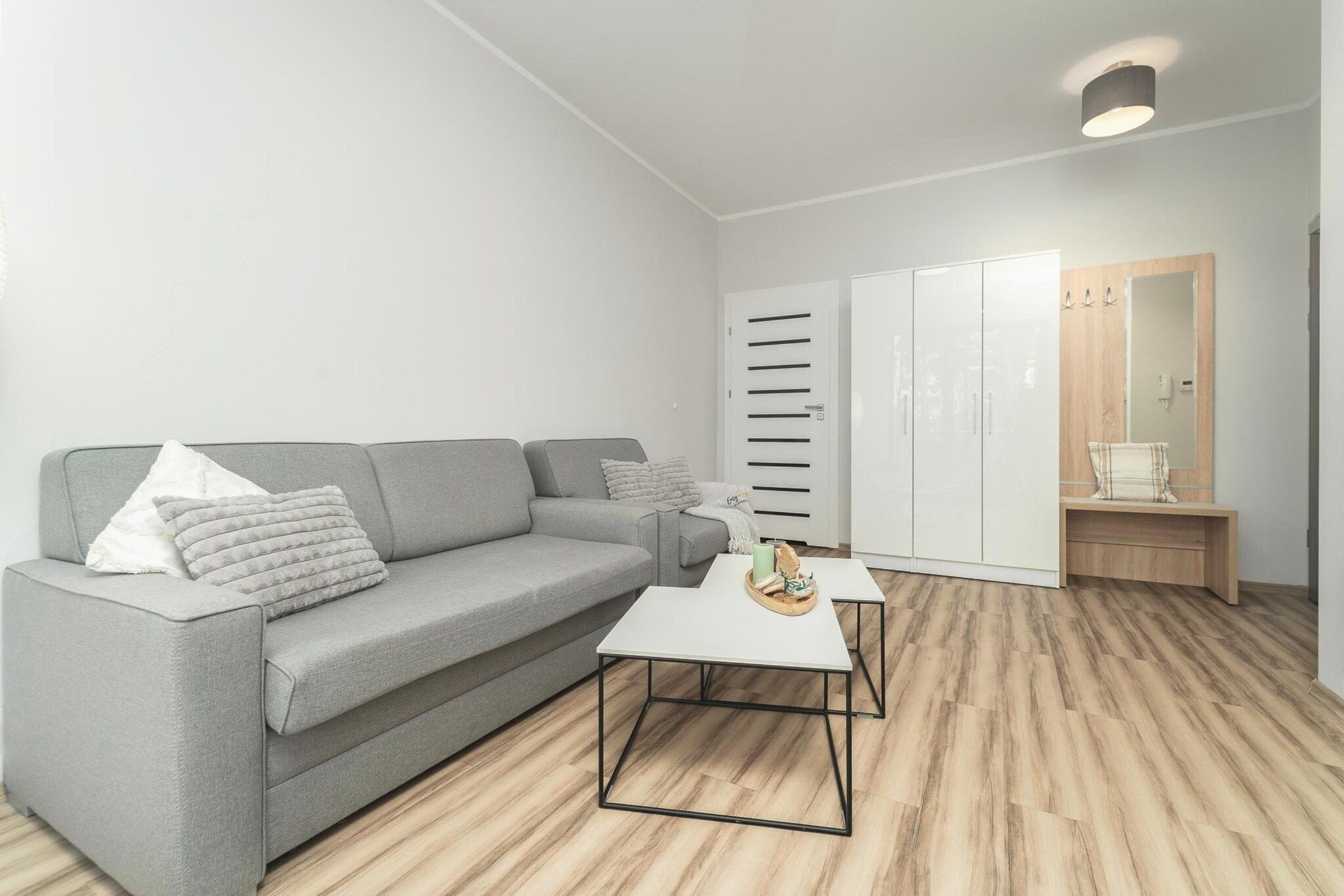 Una sala de estar moderna con un sofá gris, una mesa de centro blanca y suelo de madera.
