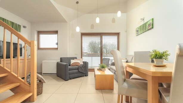 A modern living room with a sofa, a dining table, and a staircase. - Apartment in Rewal by Baltic Sea Beach (Rewal)