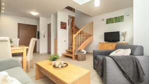 A modern living room with a sofa, a coffee table, a TV, and a staircase. - Apartment in Rewal by Baltic Sea Beach (Rewal)